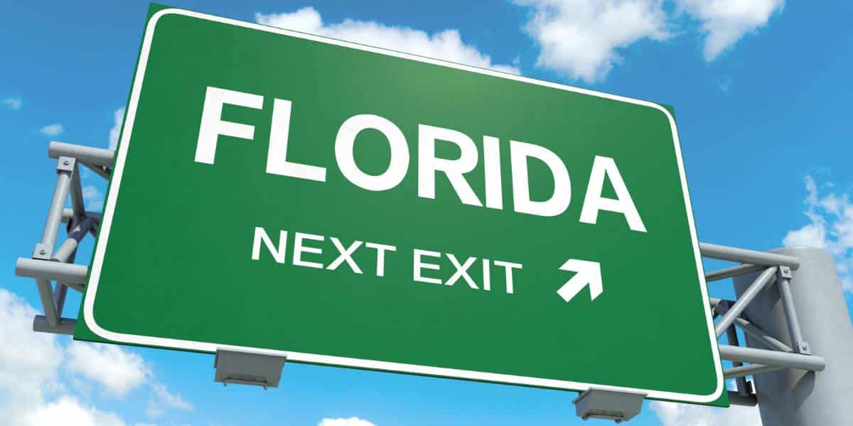 A large green road sign points toward the next exit for Florida under a clear blue sky. This image could be used to discuss Florida dash cam laws.