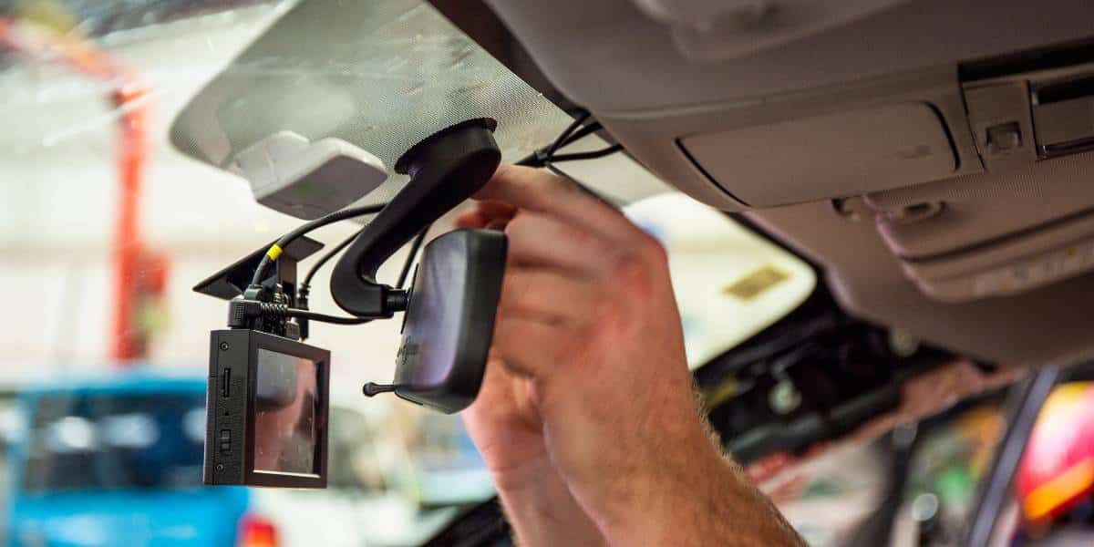 A person is installing a dash cam on the windshield of a vehicle. The device is positioned to capture dash cam footage from the front view of the car.