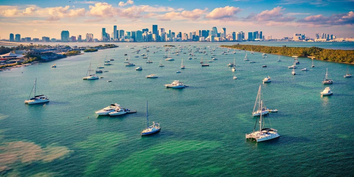 A vibrant view of boats anchored in Florida's clear blue waters with a city skyline in the background, illustrating the importance of understanding Florida boating laws for safe and responsible navigation.