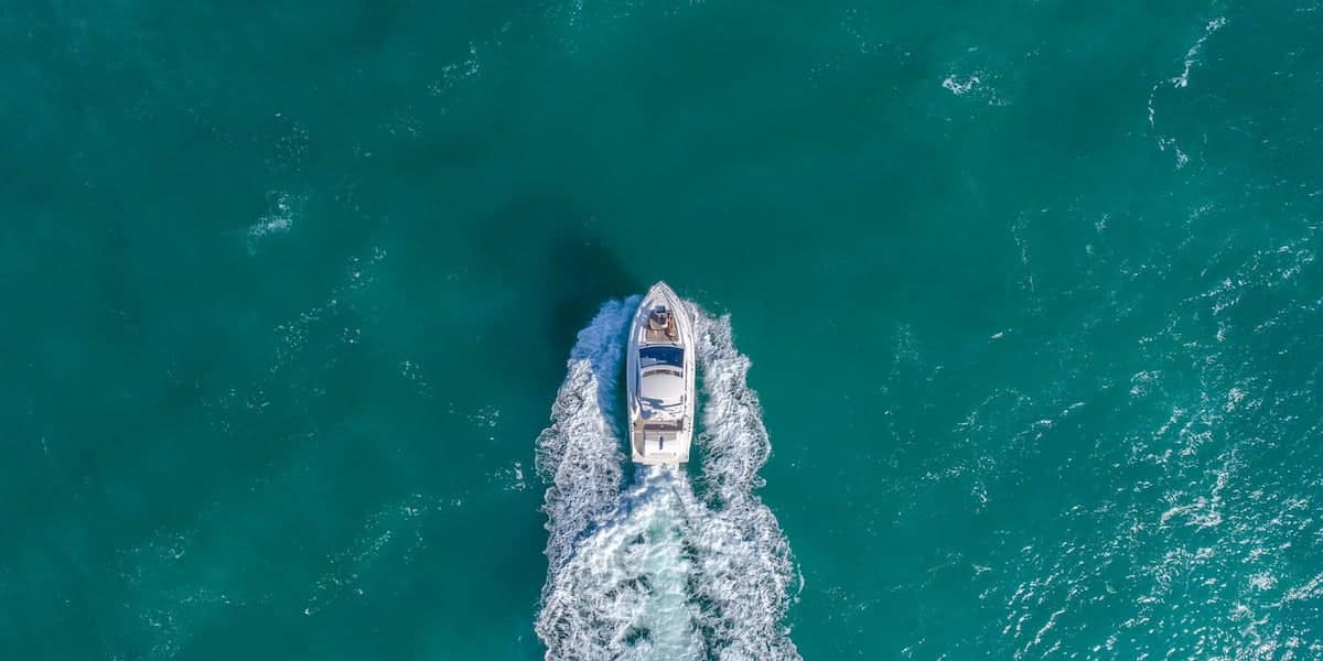 Aerial view of a boat cruising through calm turquoise waters, emphasizing the importance of knowing what is the first action required of a boat operator who is involved in a boating accident.